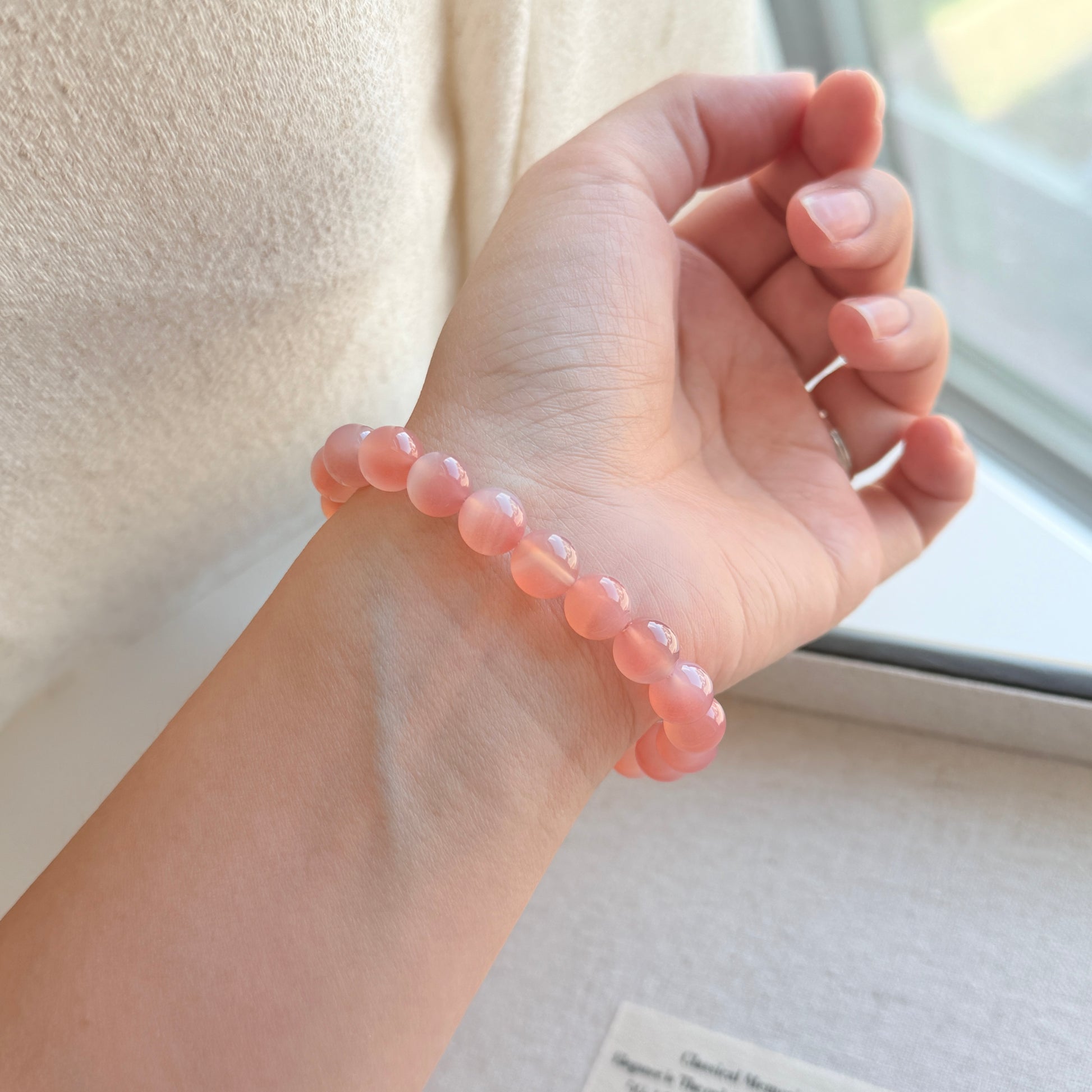 Hand wearing a pink beaded bracelet with a neutral background