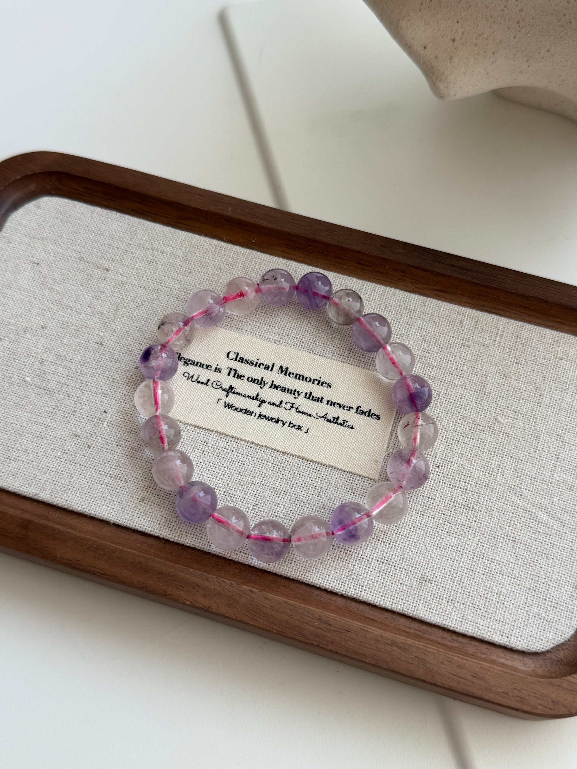 Amethyst and clear crystal beaded bracelet on a wooden tray with a card underneath