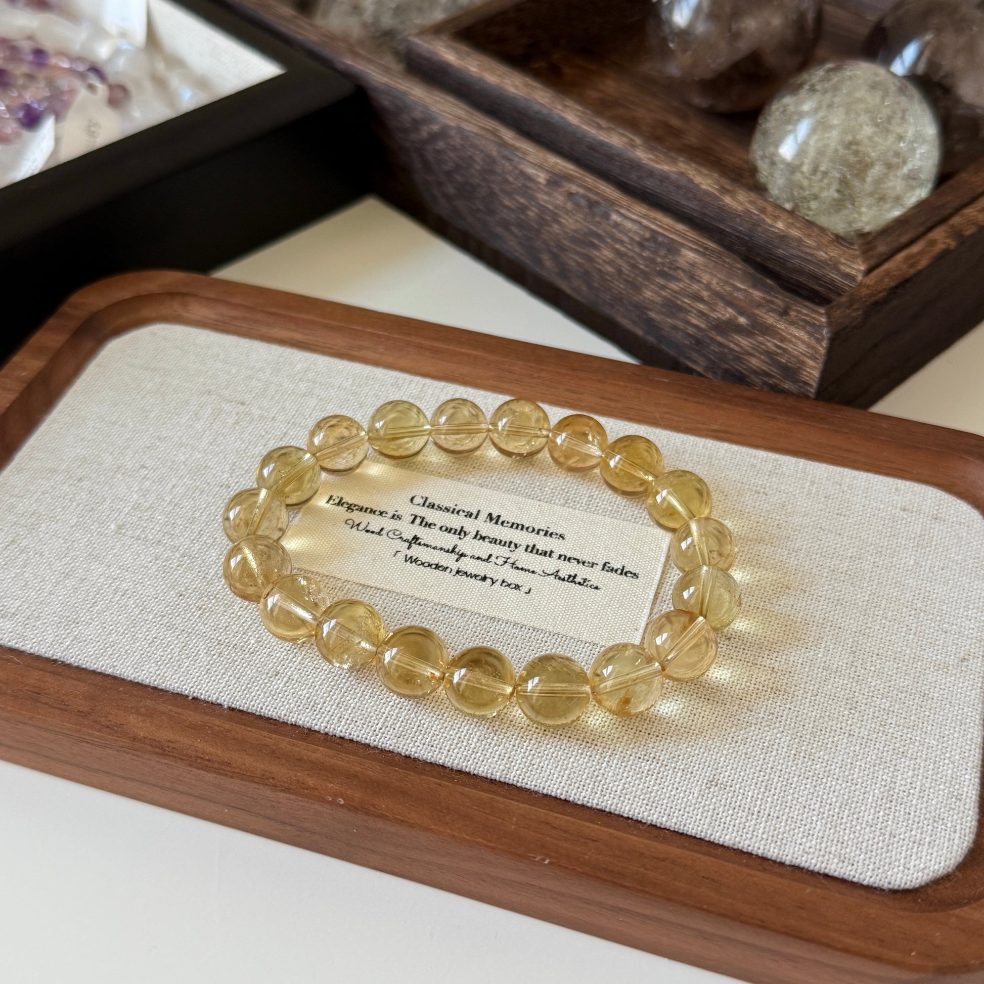 Citrine Beaded bracelet on a wooden tray with a text card, surrounded by decorative stones.