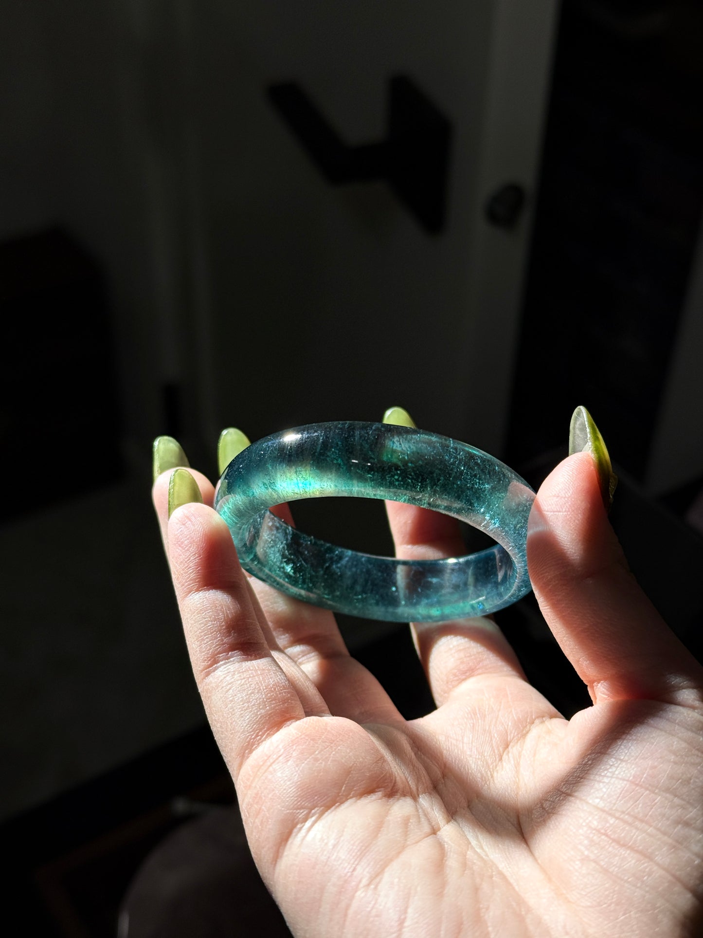 Hand holding a greenish-blue jade ring against a dark background
